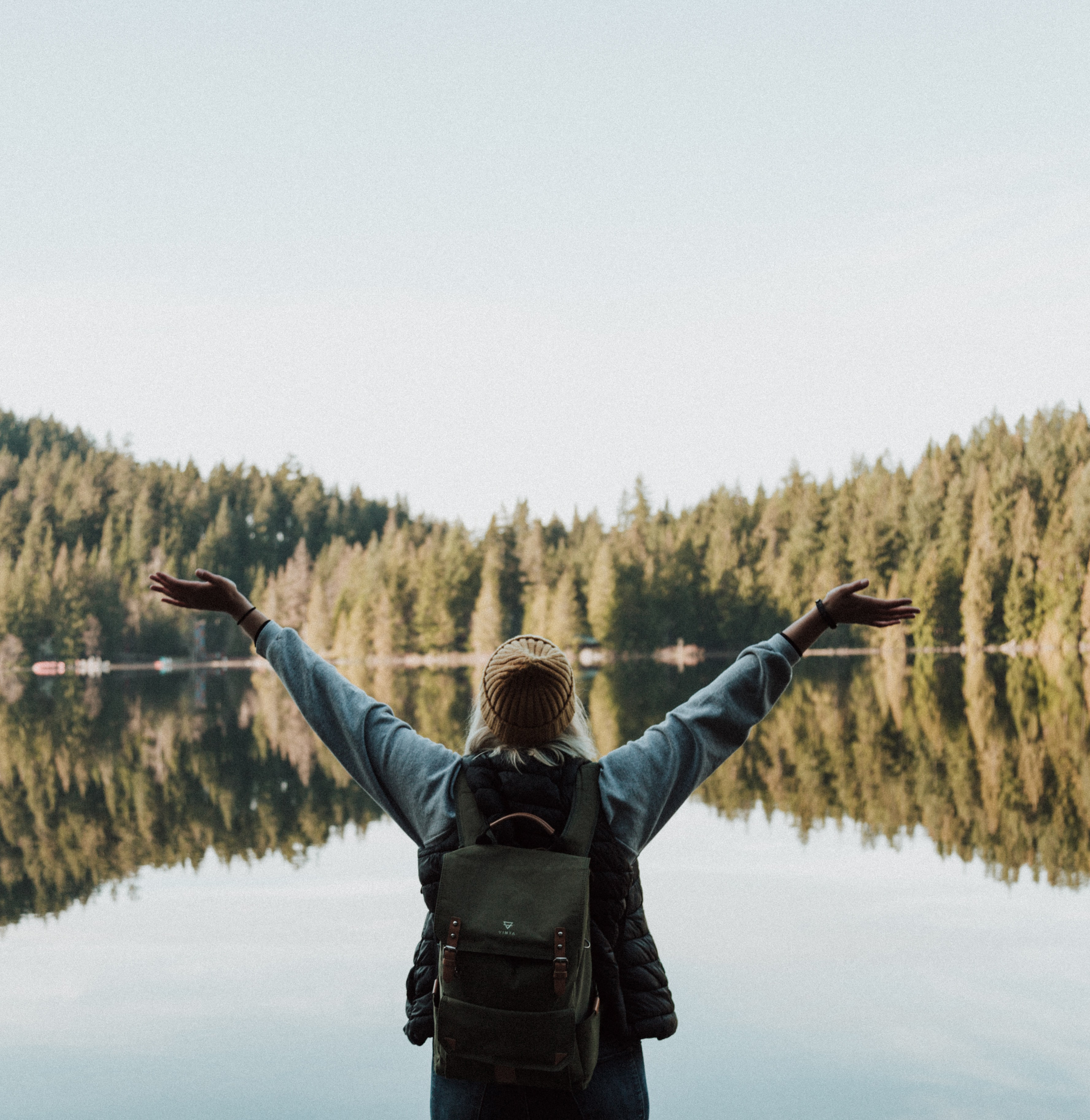 femme avec sac à dos vue de dos face à un lac avec bras levés illustrant qu'une vision accompagnée de l’action peut changer le monde 